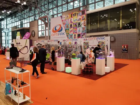 Optipak booth by Purple Exhibits: optipak island booth on orange carpet with a tall hanging banner, white pedestals