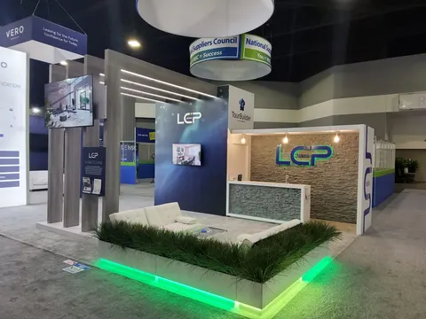 LCP trade show booth built by Purple Exhibits: LCP island booth with a wood-slat pergola, stacked stone wall with backlit logo, white lounge sofa ringed by grass and green LED floor lighting, and wall-mounted screens.
