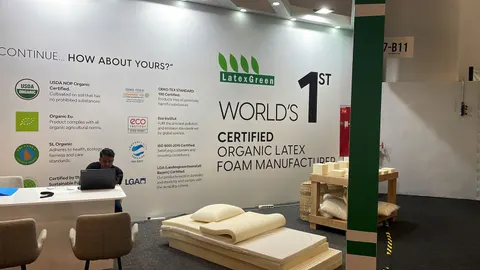 LatexGreen trade show booth built by Purple Exhibits: White inline back wall for LatexGreen with green accent stripe and 'World's 1st Certified Organic Latex Foam Manufacturer' headline, certification logos, a white coun