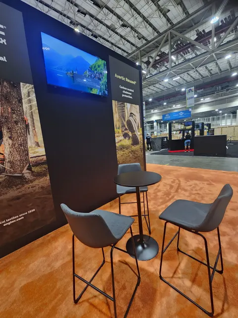 Avertic Armour trade show booth built by Purple Exhibits: Detail of a black back wall with forestry photo graphics, a wall-mounted screen showing a lake video and Avertic Armour chainsaw protection panel, with a black bi
