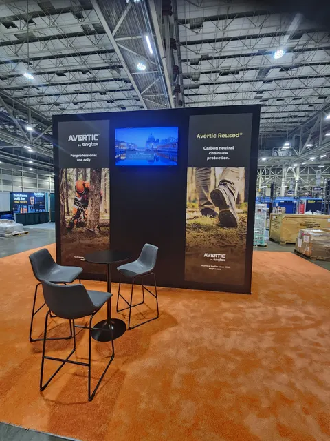 Avertic by Engtex trade show booth built by Purple Exhibits: Black inline back wall for Avertic by Engtex with two large forestry lifestyle graphics flanking a wall-mounted screen, orange carpet and a bistro table with d