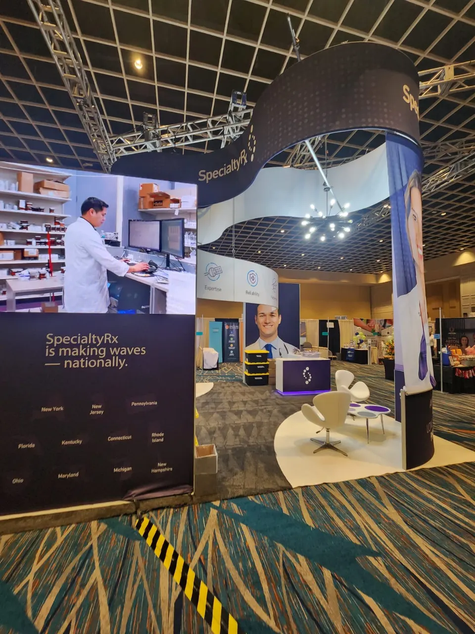 SpecialtyRx booth by Purple Exhibits: angled view of the SpecialtyRx island showing a navy wall graphic reading