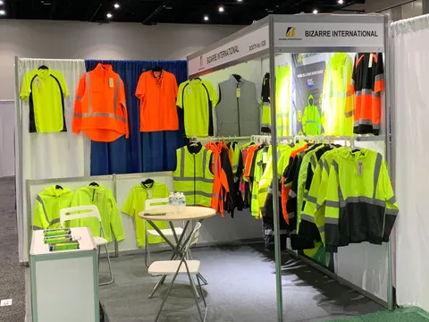 Bizarre International trade show booth built by Purple Exhibits: Small inline 10x10 booth for Bizarre International with high-visibility yellow and orange safety jackets and vests hung on white panel walls, a small round