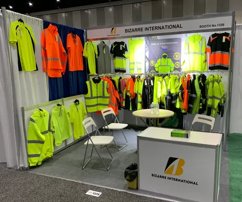 Bizarre International trade show booth built by Purple Exhibits: Bizarre International inline booth 1326 showing hi-vis safety workwear on hanging rails, a white logo counter, round table with chairs and a header sign on