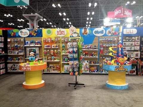 Bright Starts trade show booth built by Purple Exhibits: Colourful inline toy booth for Bright Starts, Baby Einstein and Oball with blue and yellow slatwall bays full of packaged infant toys, round yellow product pedesta