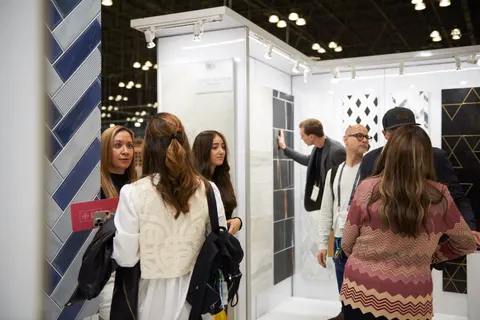 Trade show booth built by Purple Exhibits: Close-up inside a white tile showroom booth with visitors examining marble and herringbone blue tile display panels under bright track lighting.