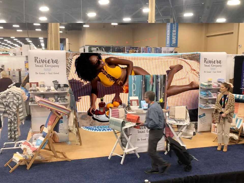 Riviera Towel Company booth by Purple Exhibits: inline booth with a large beach-scene photo back wall of a woman, one of our builds to compare for MANTS