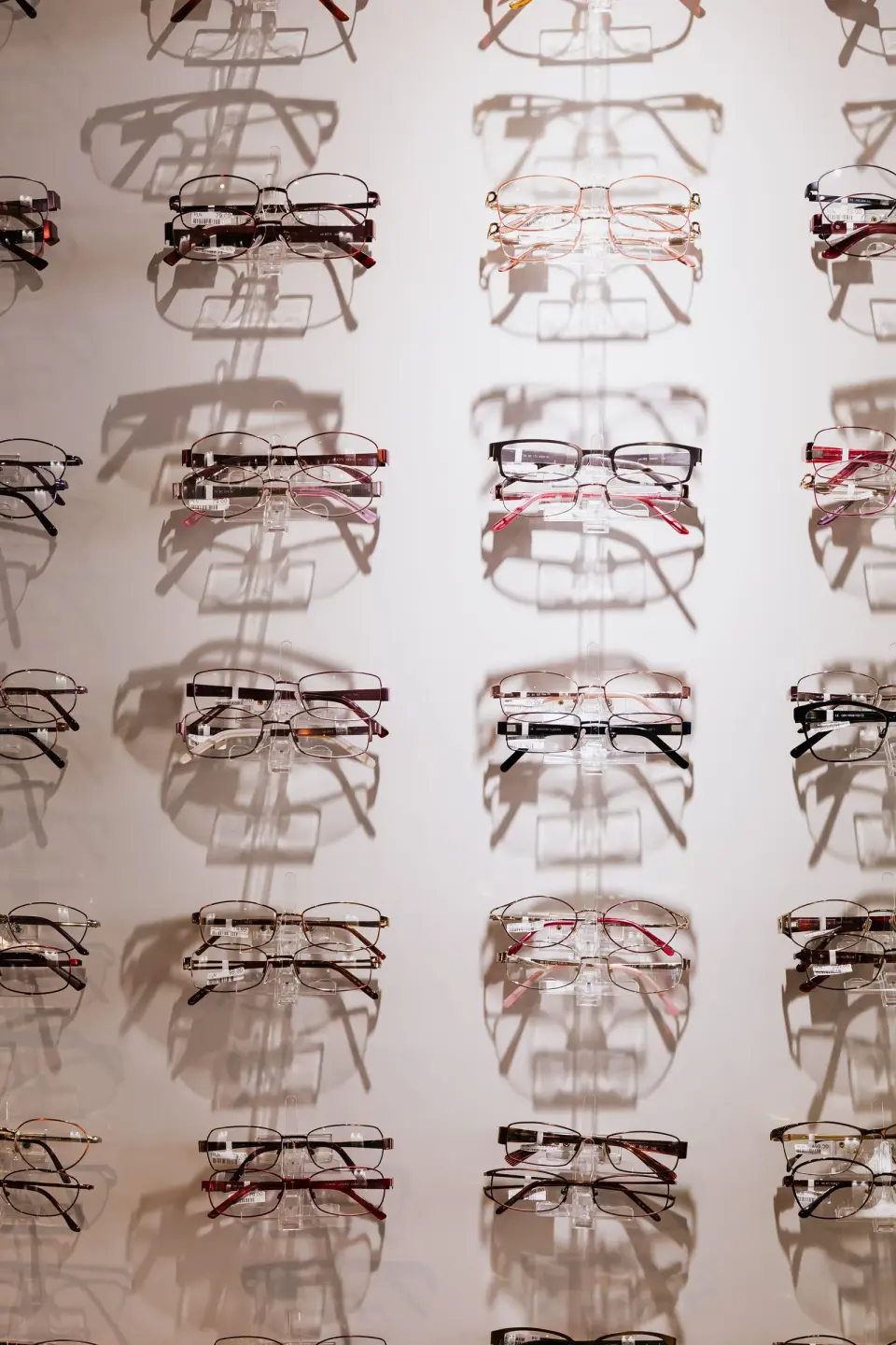 Rows of eyeglass frames on a white lit display wall casting soft shadows