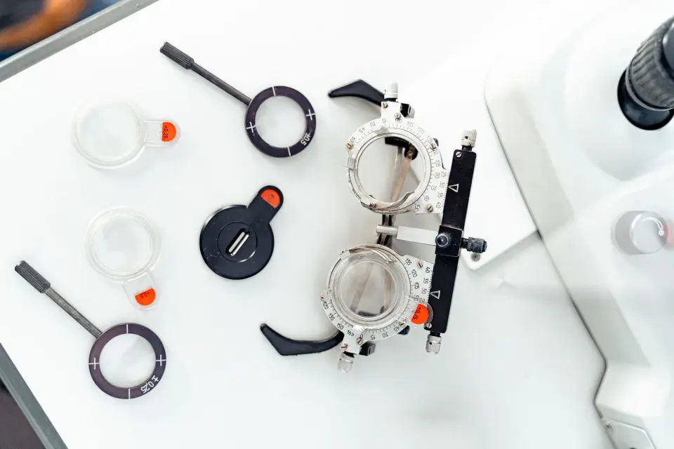 Trial frame, trial lenses and an occluder laid out on a white table beside an eye testing instrument