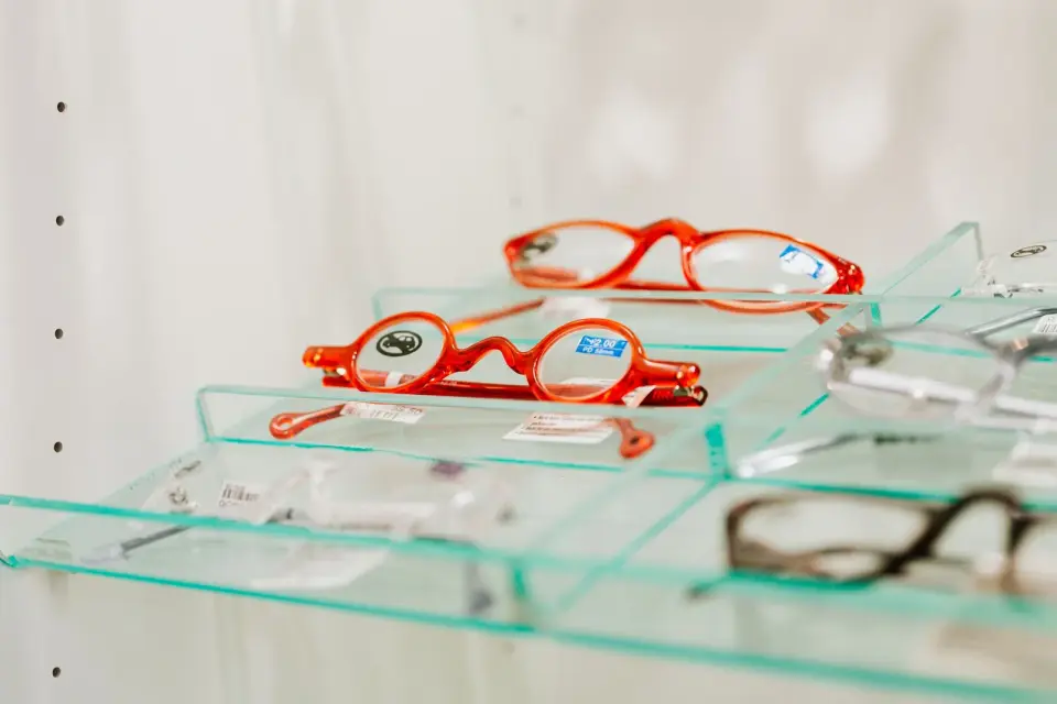 Red and tortoiseshell eyeglass frames on clear glass shelves in an optical store