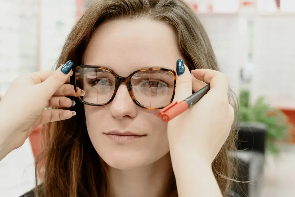 Optician fitting tortoiseshell eyeglasses and marking lens centers on a client