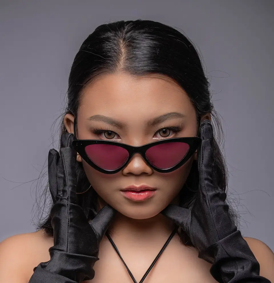 Woman in black cat-eye sunglasses with rose lenses and satin gloves, studio fashion portrait