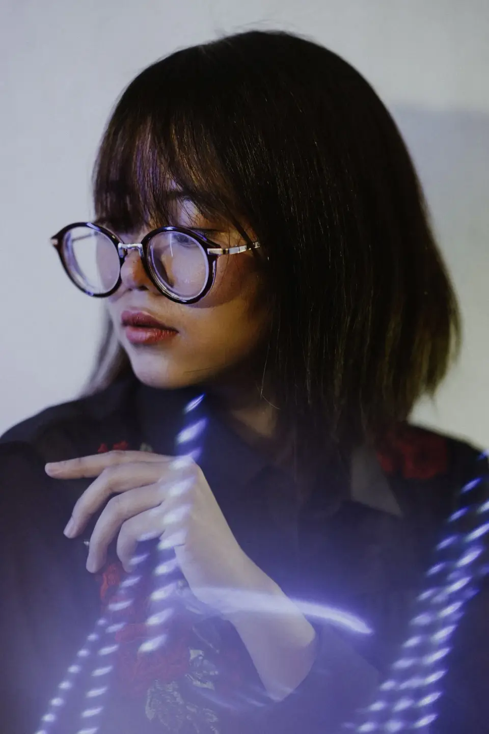 Woman in round dark eyeglass frames with soft light trails, editorial portrait