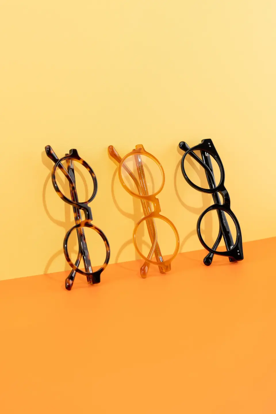 Three round eyeglass frames in tortoiseshell, amber and black acetate on orange