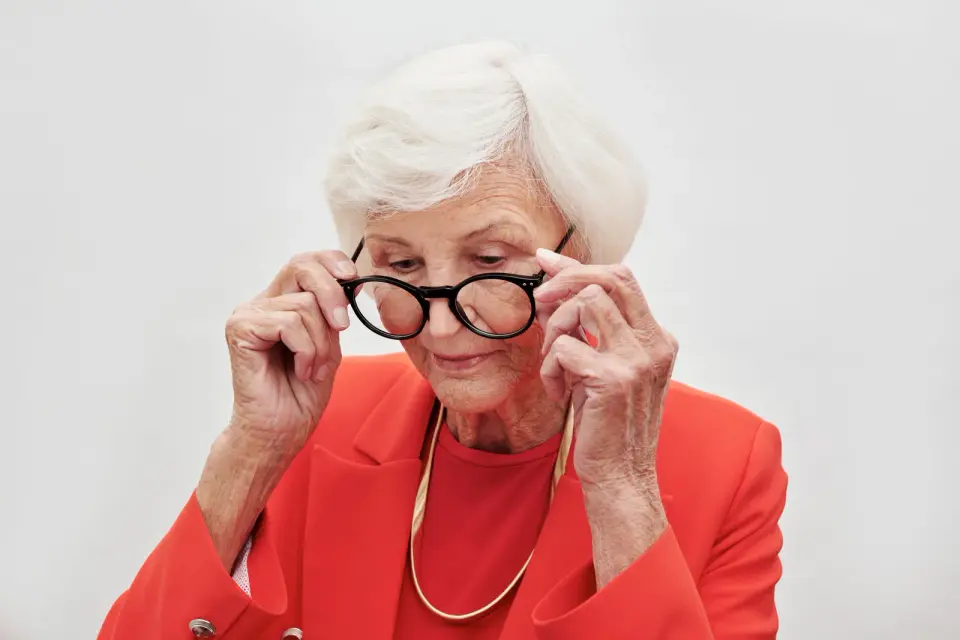 Silver-haired woman in a red blazer adjusting round black eyeglass frames