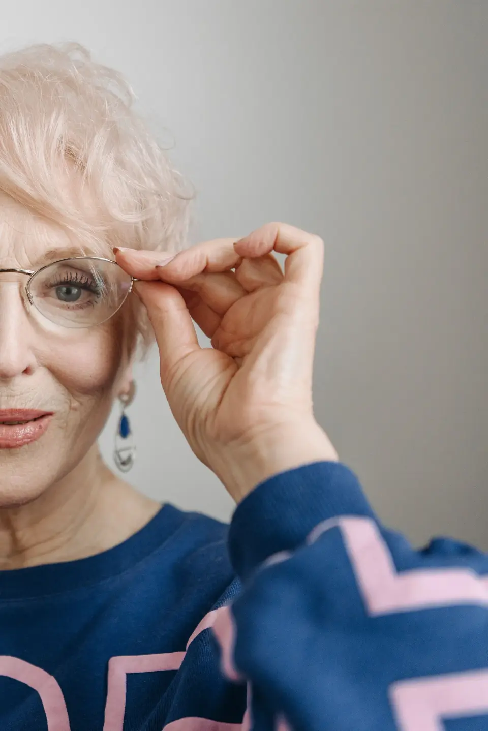 Older woman adjusting slim metal eyeglasses, close-up portrait