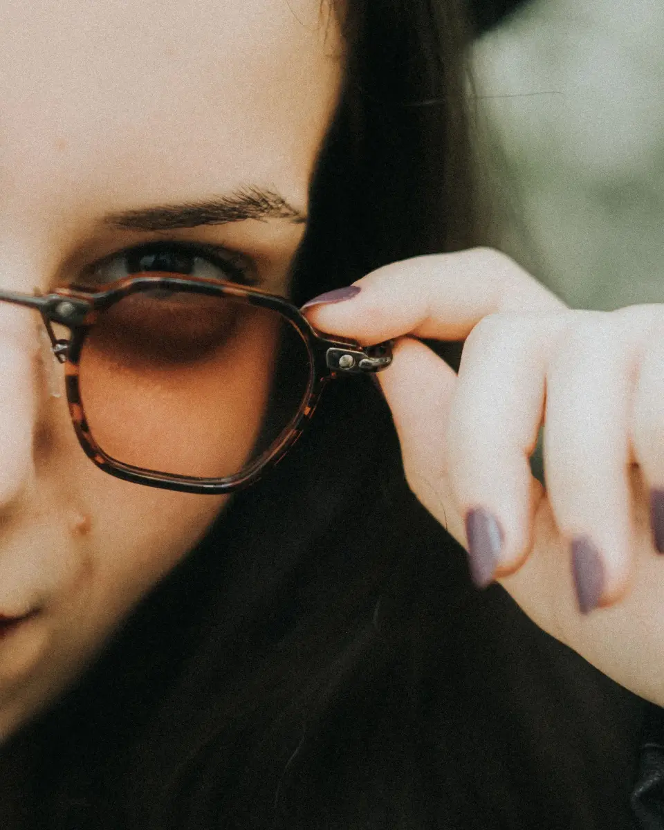 Close-up of a hand adjusting tortoiseshell frames with amber tinted lenses