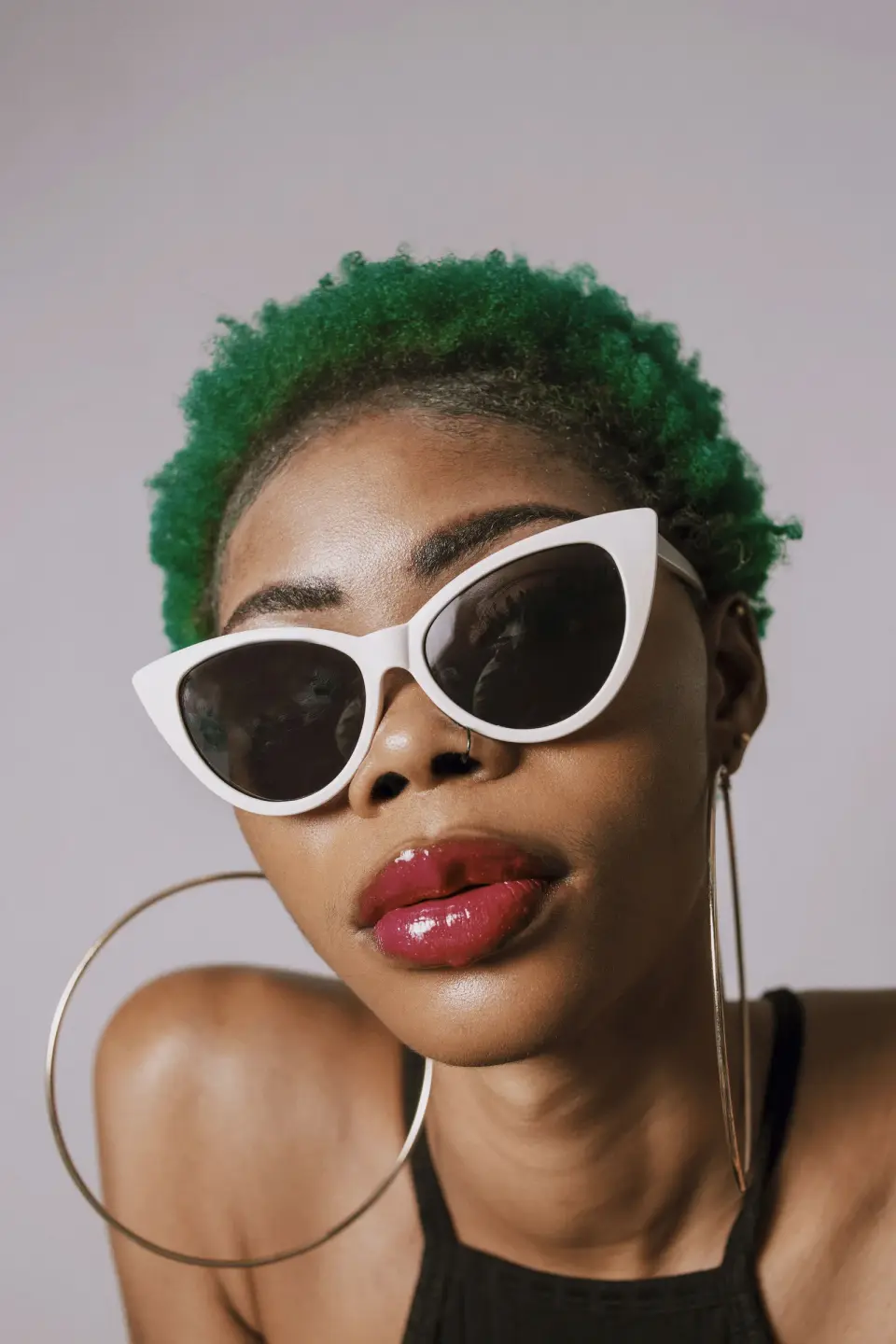 Woman with green hair in white cat-eye sunglasses and hoop earrings, studio portrait
