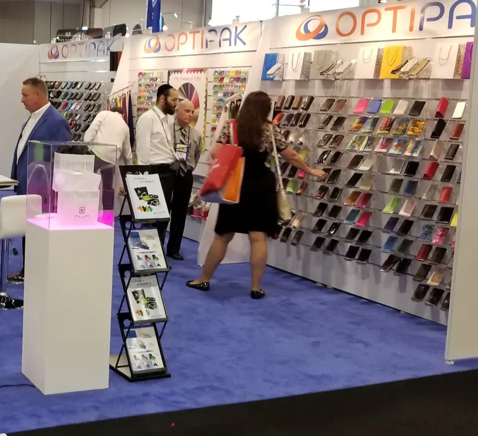 Optipak booth by Purple Exhibits with a long slatwall of eyewear cases in many colors, a lit pedestal and a literature rack, with visitors browsing