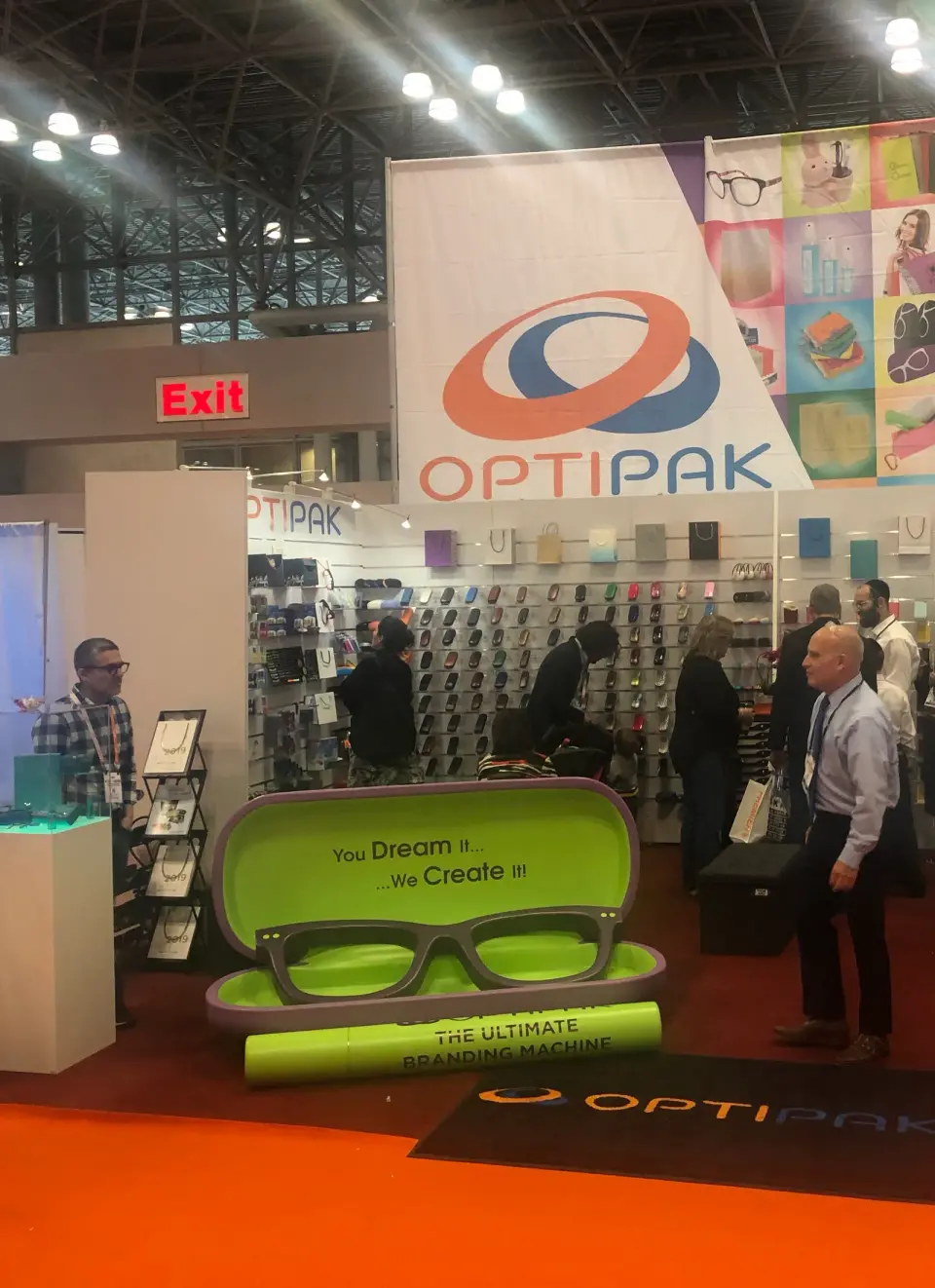 Optipak booth by Purple Exhibits with a large printed banner, a giant open eyewear case display and a wall of cases behind