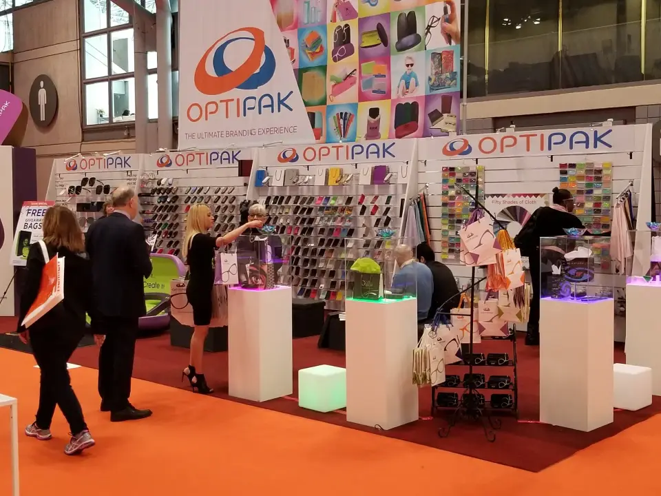 Optipak booth by Purple Exhibits on orange carpet with a tall hanging banner, case walls and lit pedestals