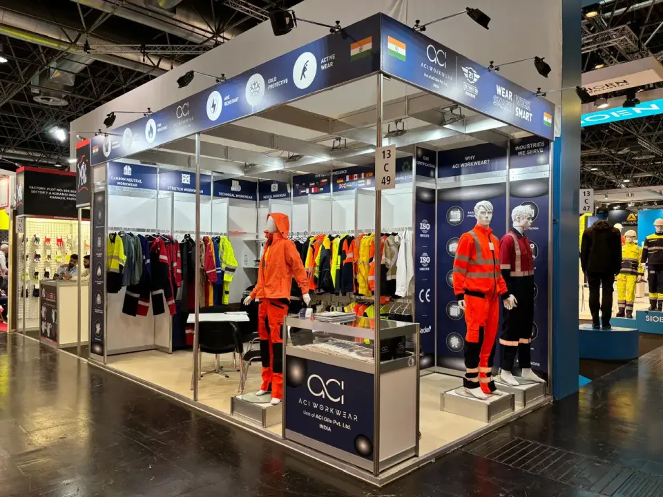 ACI Workwear booth by Purple Exhibits with high-visibility workwear on mannequins and plinths, a full rail of jackets, a lit blue header and a glass display case at the aisle