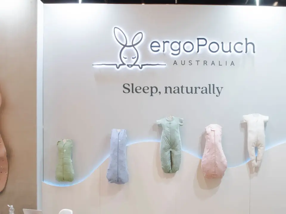 ergoPouch booth by Purple Exhibits with a lit logo wall and sleep suits hung on a curved line