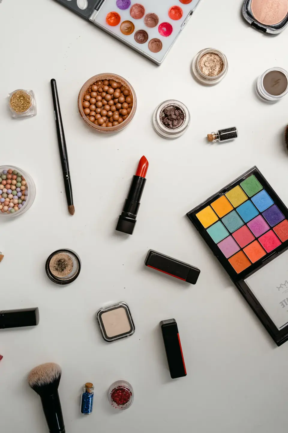 Bright eyeshadow palette, red lipstick, brushes and pressed powders on a white surface