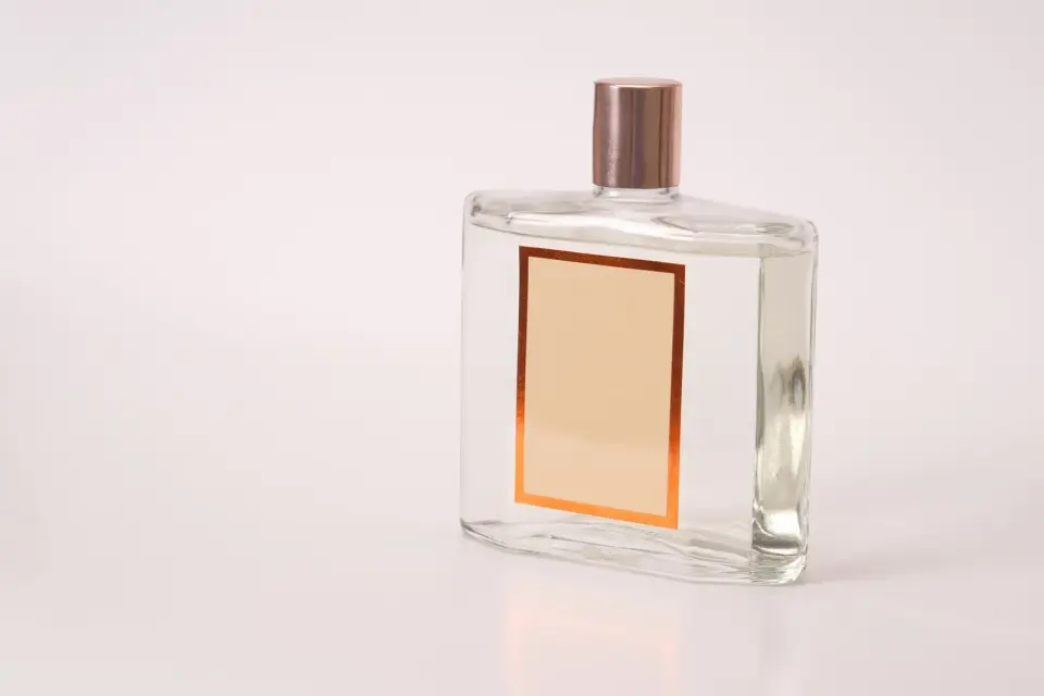 A clear glass fragrance bottle with a blank label on a pale pink background