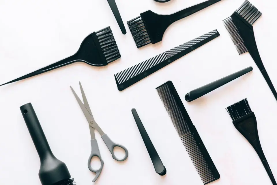 Hairdressing scissors, combs, color brushes and clips laid out on a white surface