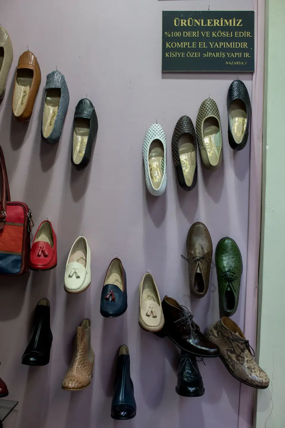 Handmade leather shoes in green, cream and red hung on a violet wall