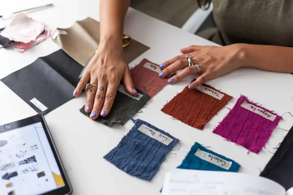 A designer sorts labeled fabric swatches in rust, pink, blue and teal on a white table