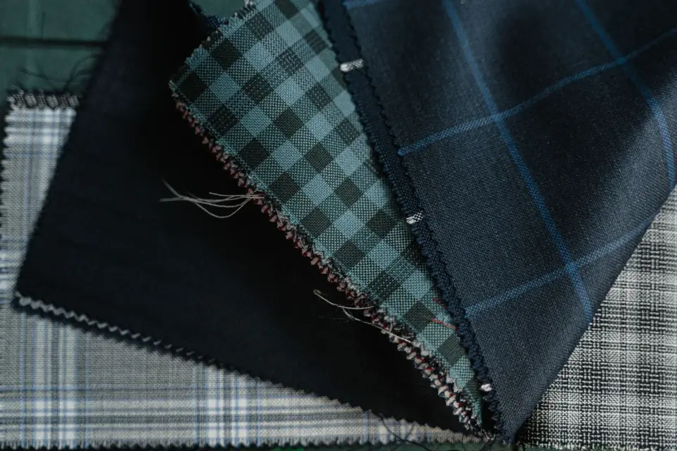 Close-up of layered wool suiting swatches in navy, green check and gray plaid