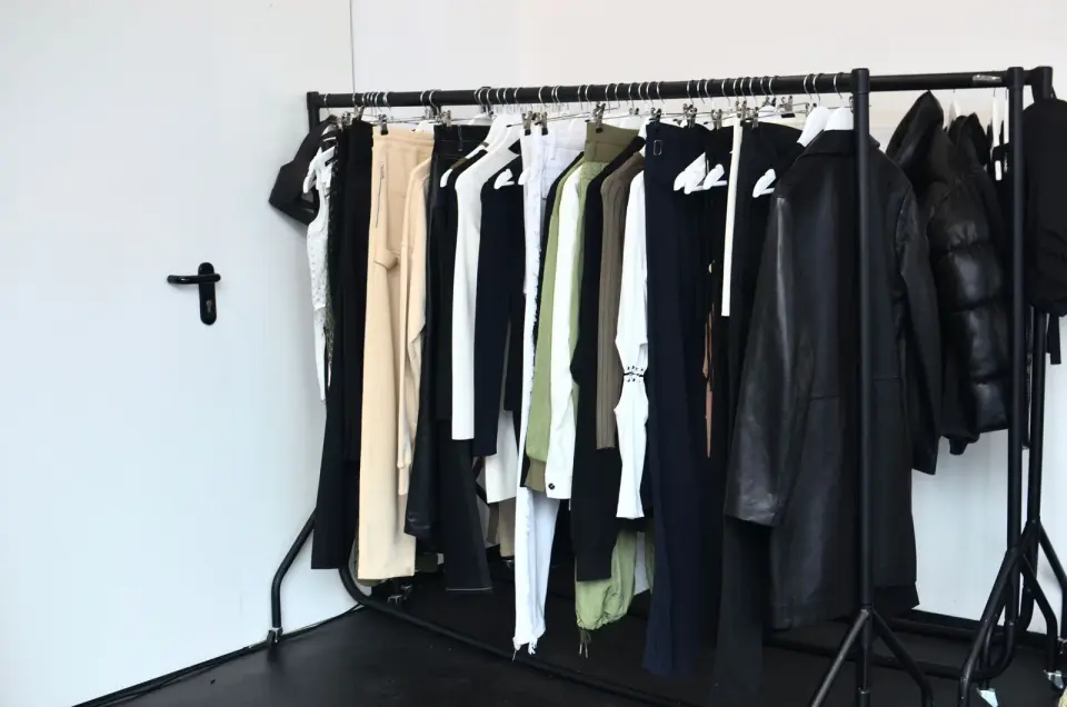Trousers, shirts and jackets on a black clothing rack against a white wall