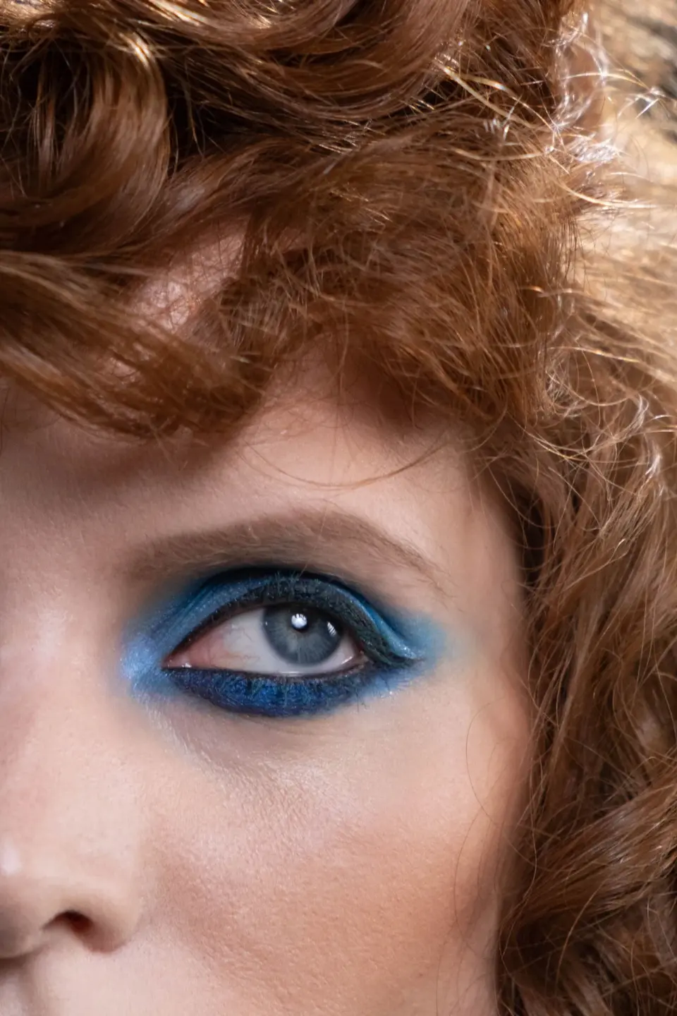 Close-up of a blue eye with bright blue eyeshadow framed by red curls