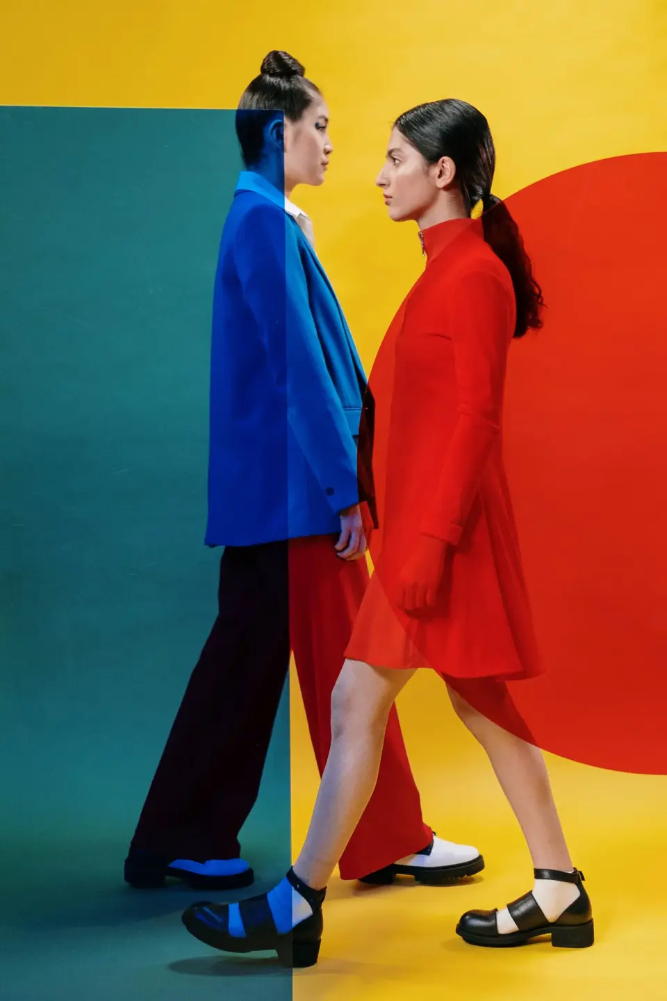 Two models in a cobalt blazer and a red dress walking past a color-blocked set