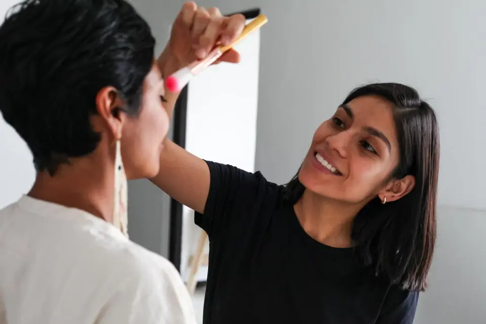Makeup artist smiling as she applies blush to a model with a brush