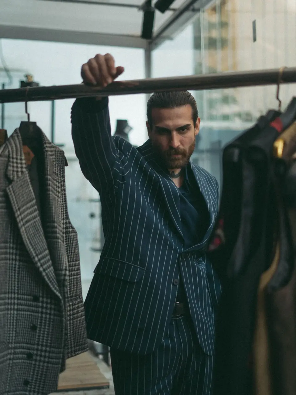 Man in a navy pinstripe suit beside a rail of tailored coats