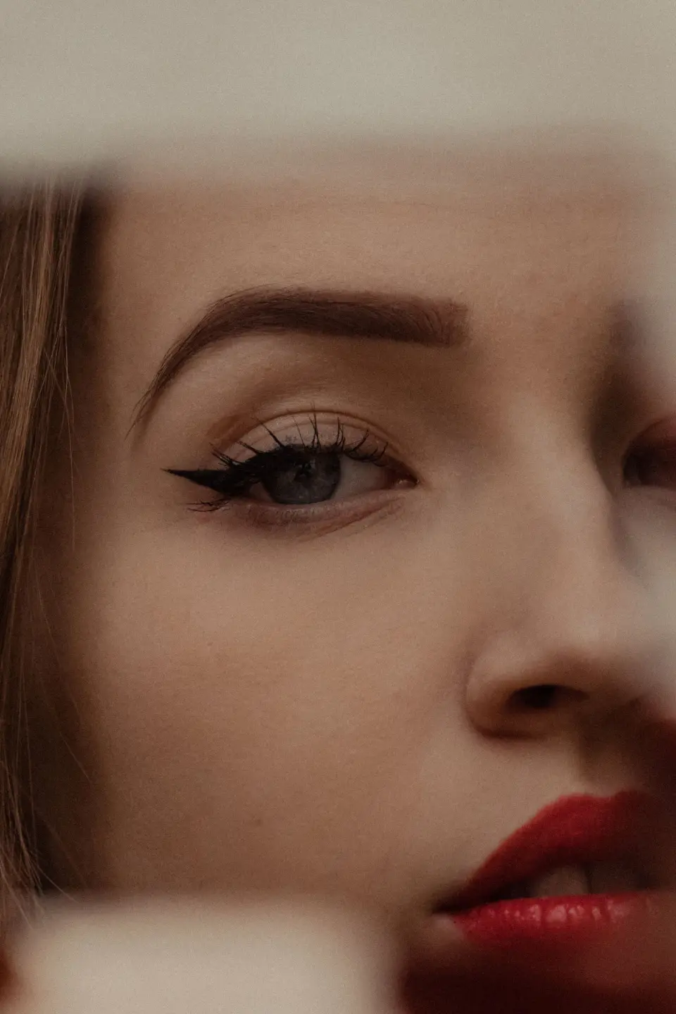 Woman with winged eyeliner and red lipstick seen past the edge of a mirror