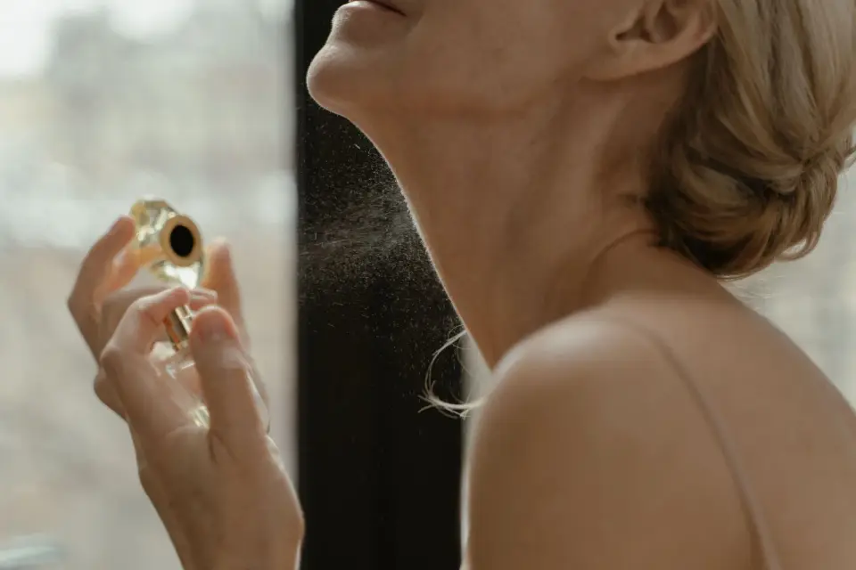 Woman spraying a fine mist of perfume at her neck from a gold-capped bottle