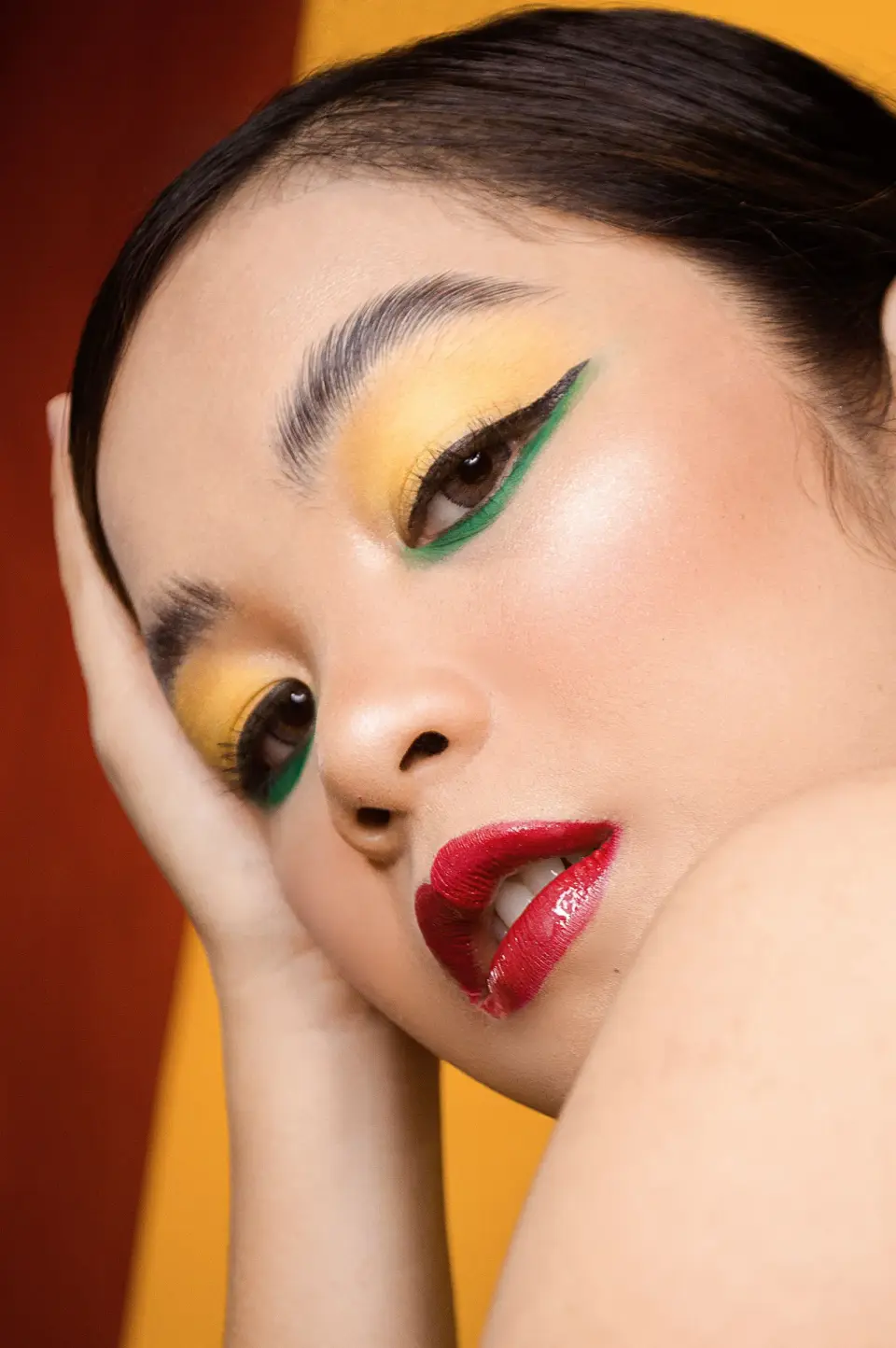 Close-up of a woman with yellow eyeshadow, green liner and glossy red lips