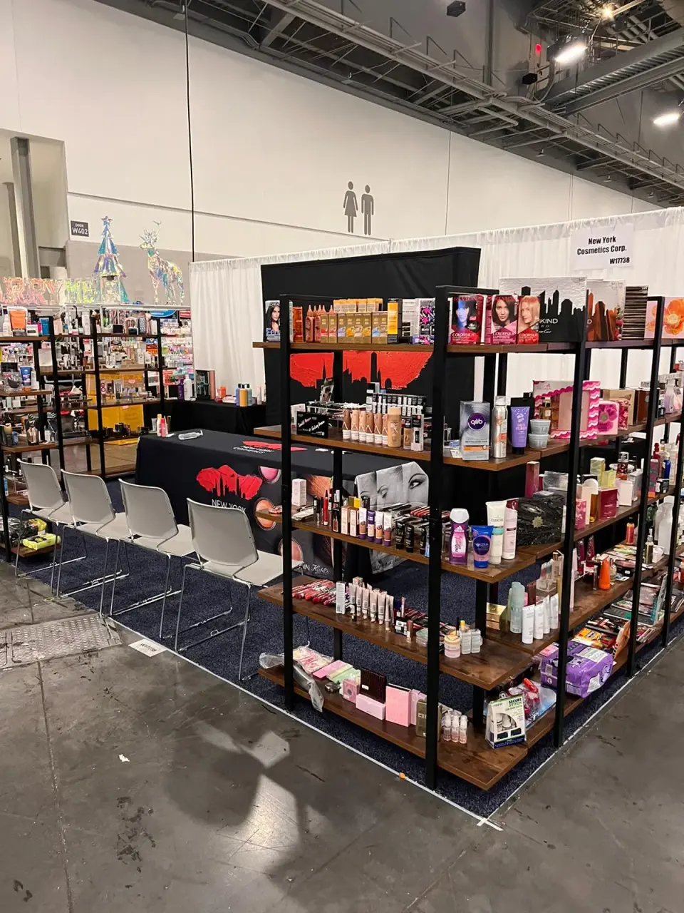New York Cosmetics booth by Purple Exhibits with open metal and wood shelving stacked with cosmetics, hair color and skincare, a draped table with chairs and a blue carpet