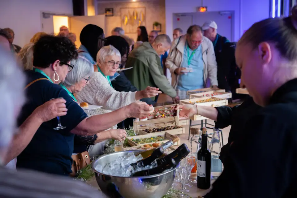 Event guests with lanyards sampling small bites from wooden crates at a catered tasting table
