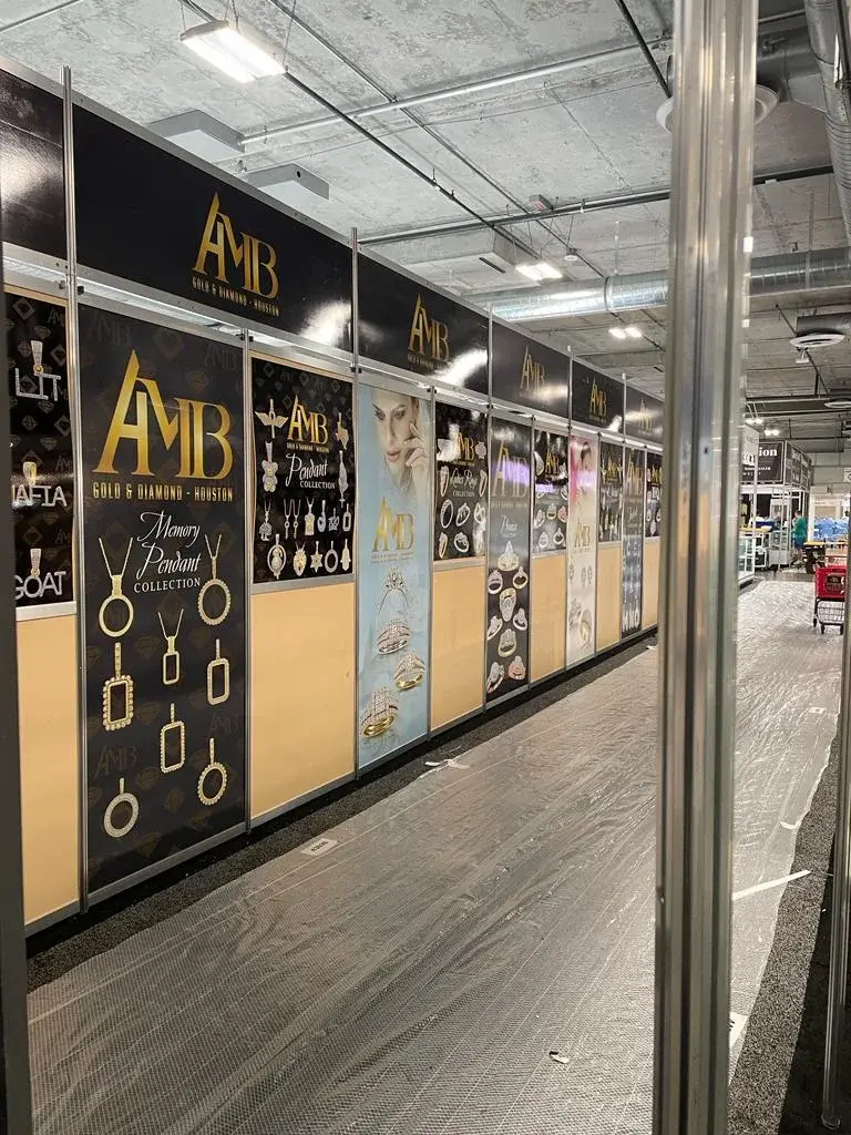 AMB Gold & Diamond booth by Purple Exhibits with a long run of black and gold collection panels for pendants and rings under a gold header