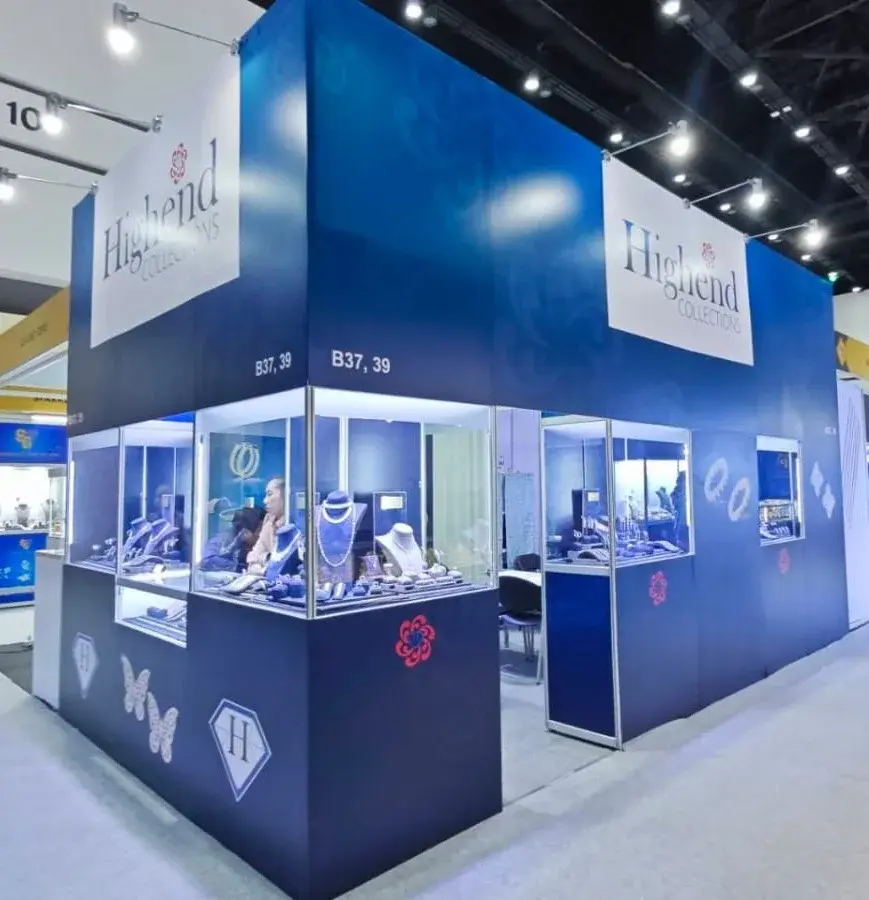 Highend Collections jewelry booth by Purple Exhibits with navy walls, lit glass showcases on two sides, necklaces on blue busts and white Highend Collections header panels