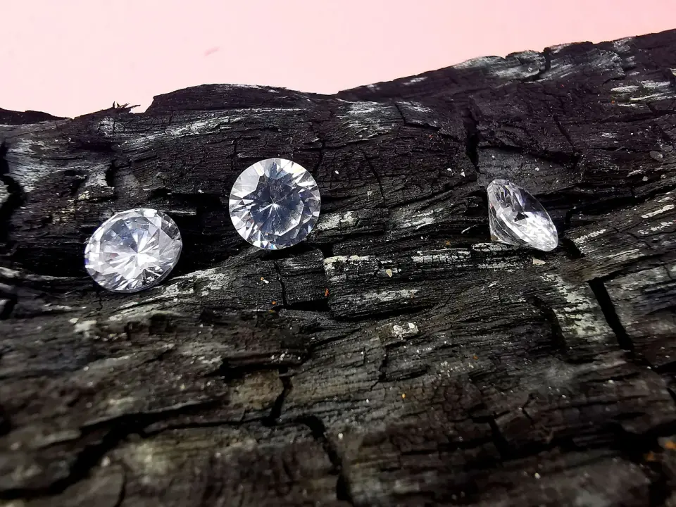 Three round and pear cut diamonds resting on a piece of dark charcoal