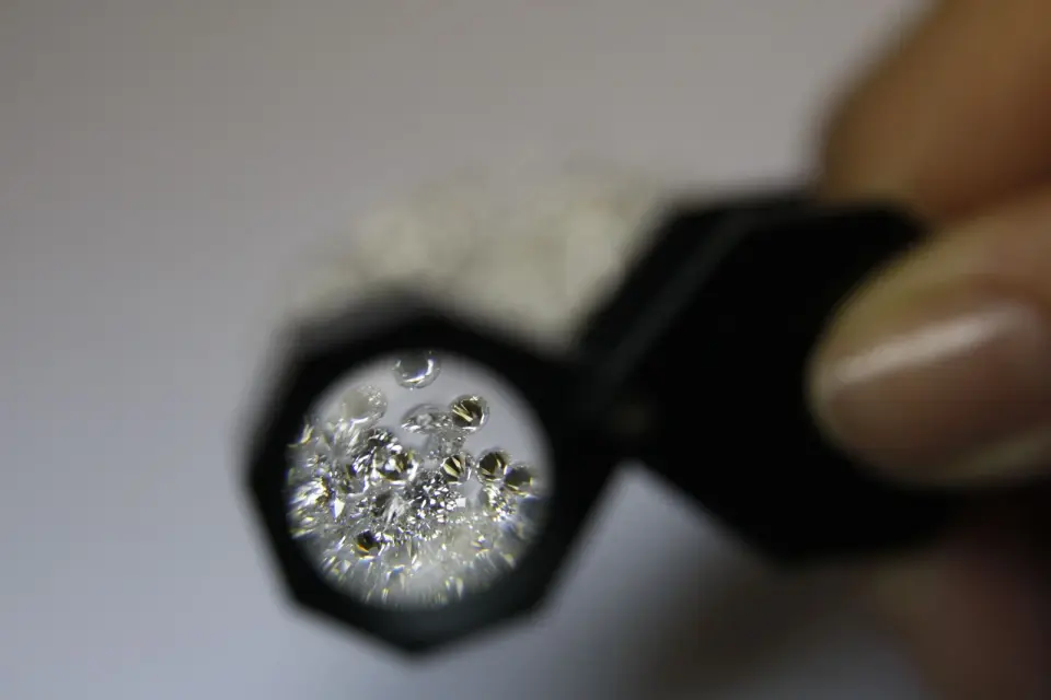 A jeweler holds a loupe over a pile of small loose diamonds