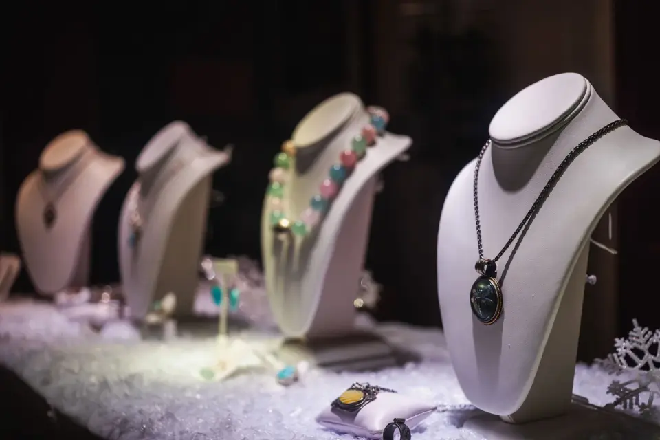Necklaces with colored stones displayed on white busts in a lit jewelry case