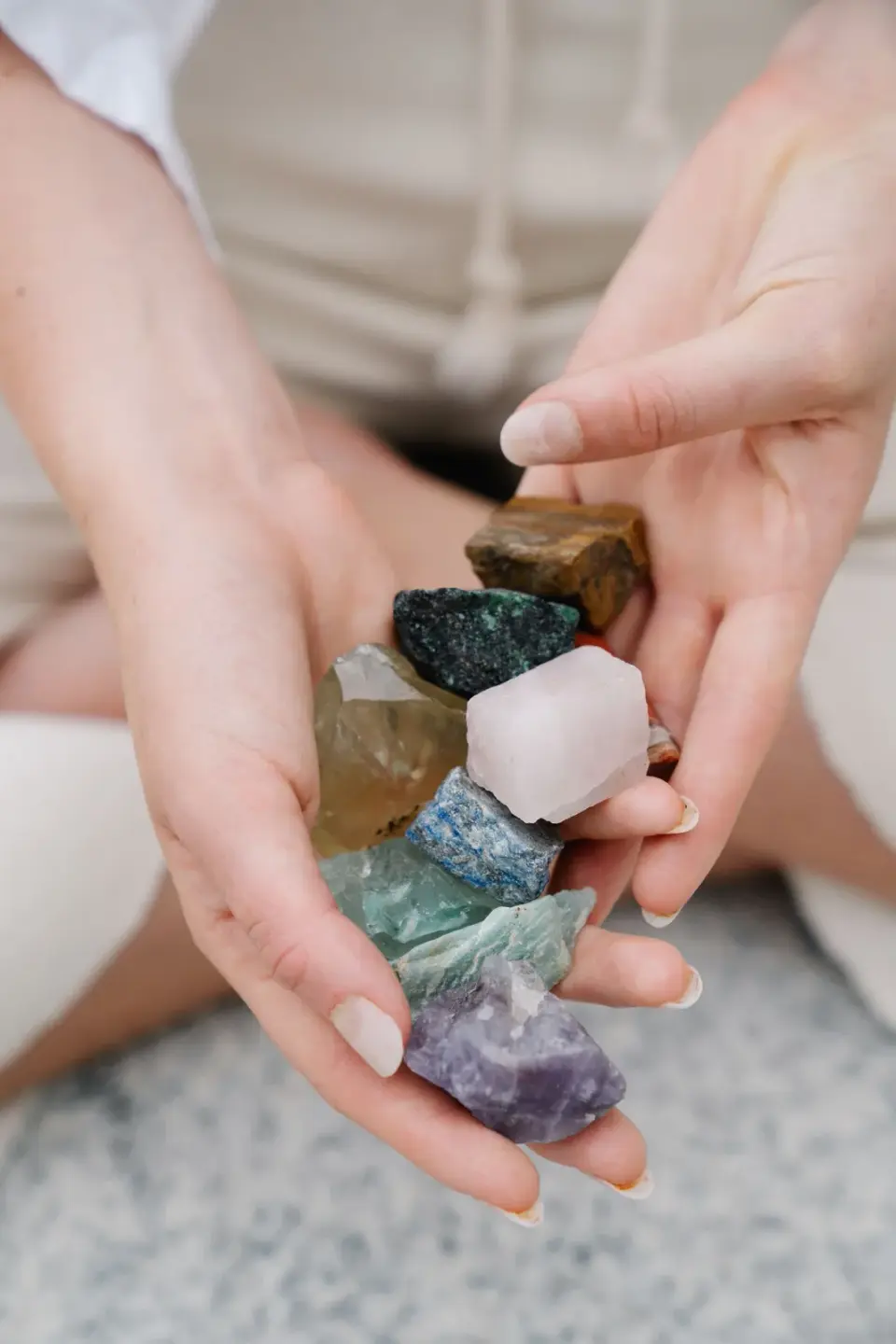 Two hands holding a stack of rough colored stones, from quartz to amethyst