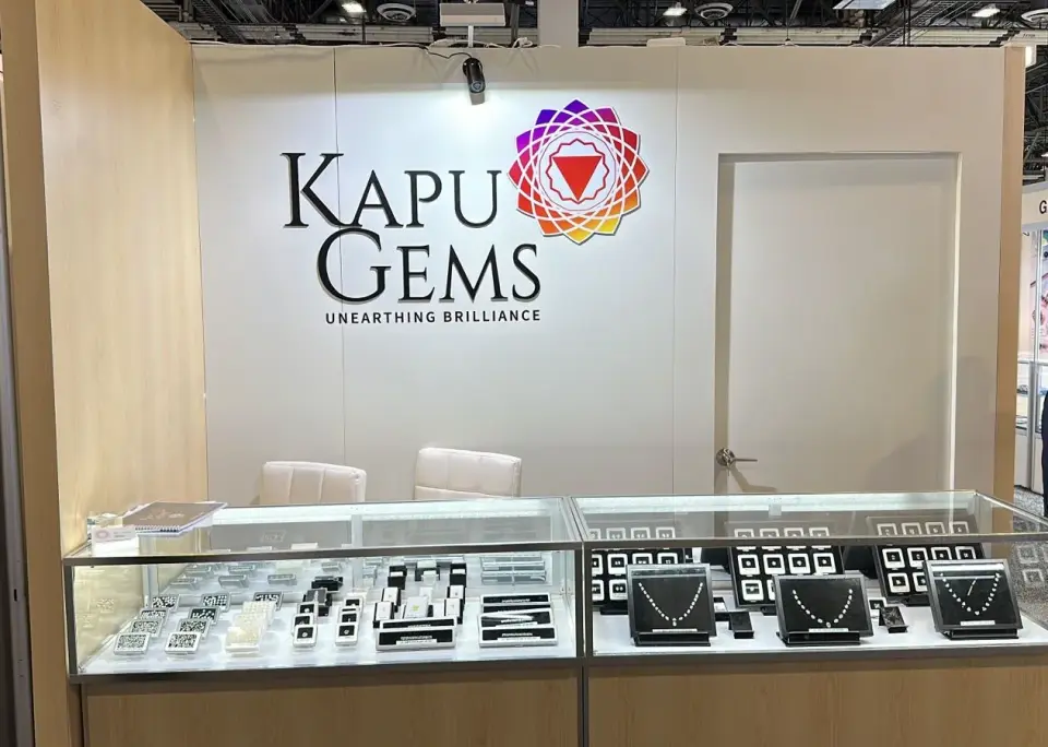 Kapu Gems booth by Purple Exhibits with two lit glass showcases of loose diamonds and necklaces in front of a white wall with the Kapu Gems logo